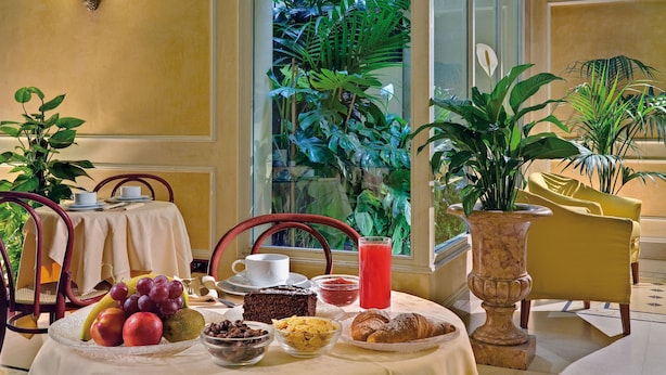 A breakfast table with fruits, pastries, and a drink, set against a window with a view of greenery. - Corona D'italia (Florence)
