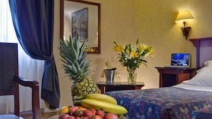 A hotel room with a bed, a desk with a computer, a fruit bowl, a vase with flowers, and a lamp. - Corona D'italia (Florence)