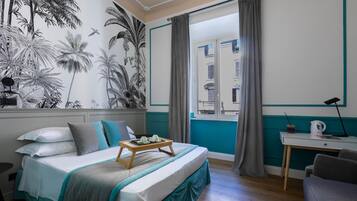 Et soveværelse med seng, et vindue med gardiner, et skrivebord med lampe og en væg med et tropisk mural.