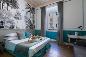 Une chambre à coucher avec un lit, une fenêtre avec des rideaux, un bureau avec une lampe et un mur orné d’une fresque aux motifs tropicaux.