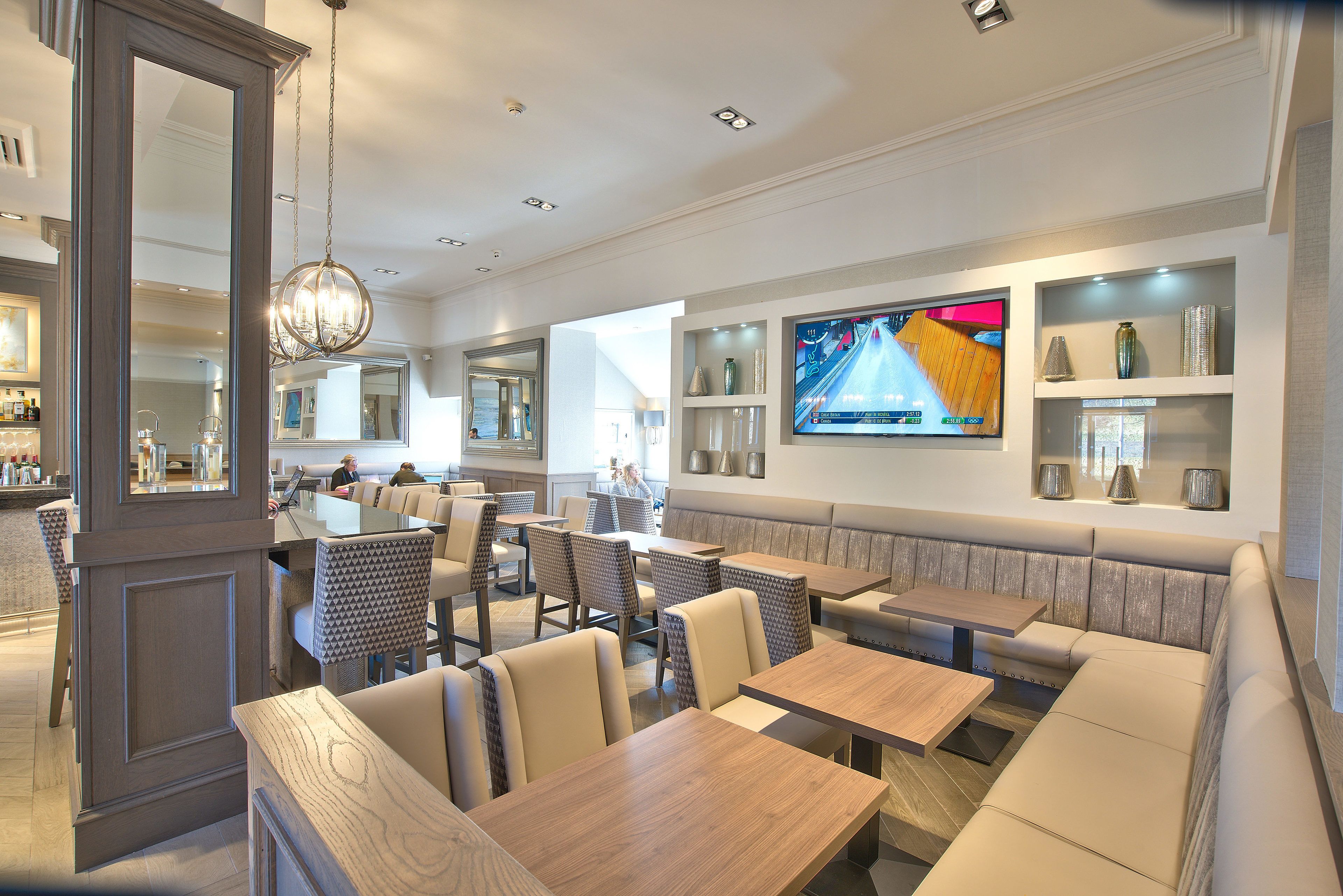 Een modern restaurant met zitjes, tafels en een groot televisiescherm waarop een bowlingwedstrijd te zien is.