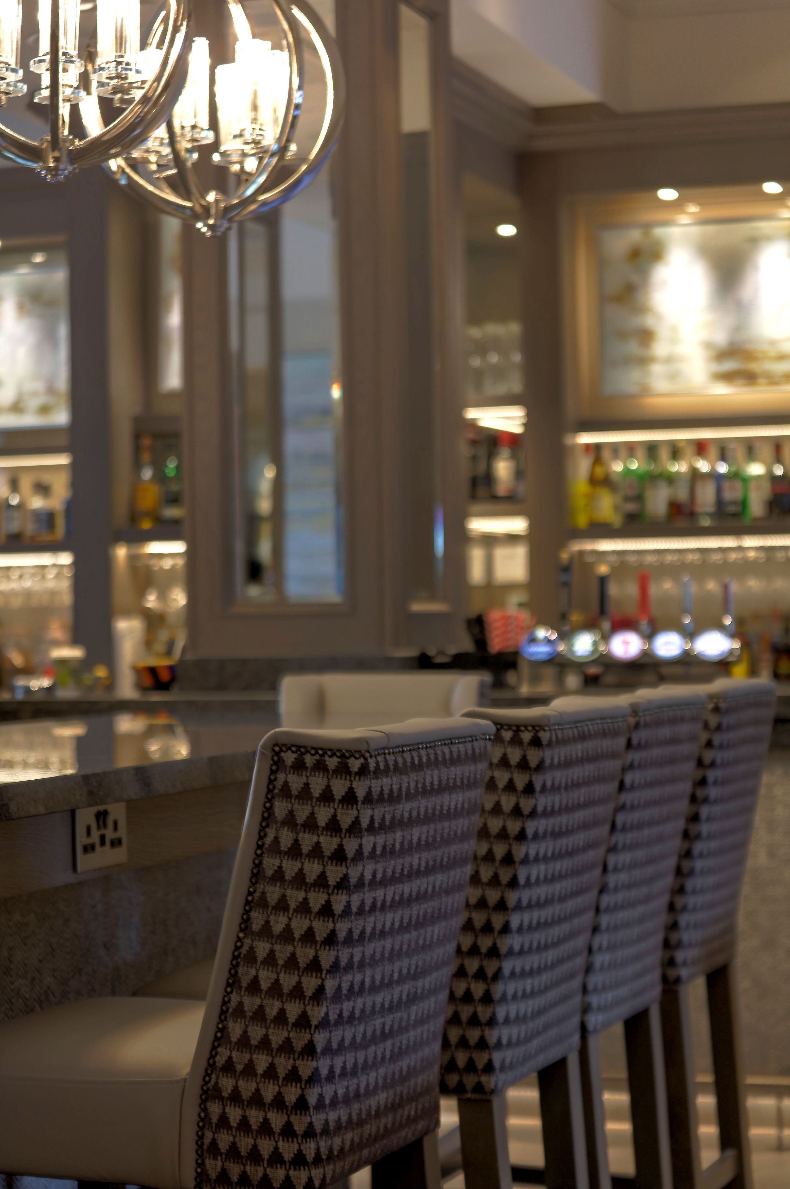 A bar area with a patterned chair in the foreground and a bar counter with various bottles in the background.