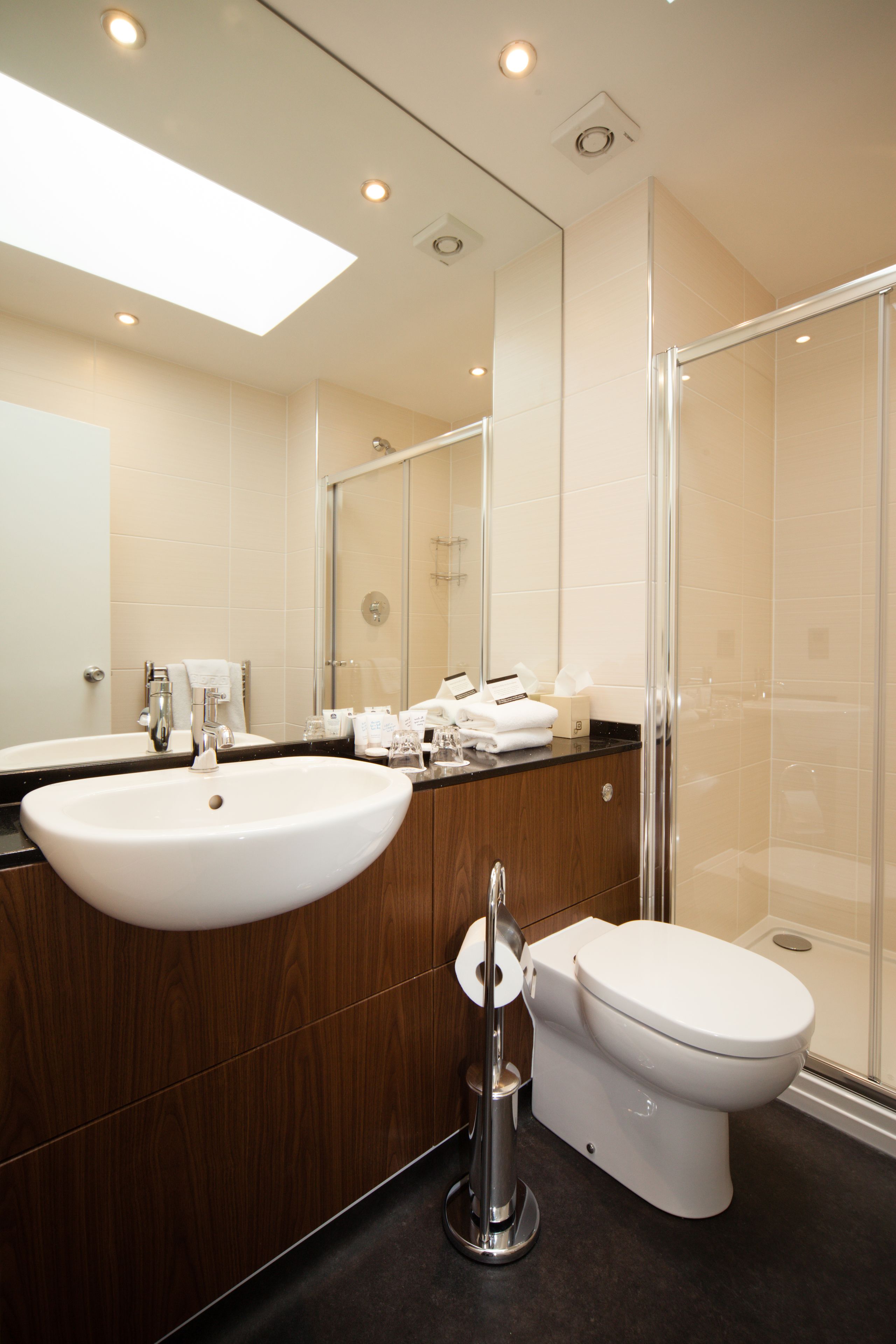 A modern bathroom with a large mirror, a sink, a toilet, and a glass-enclosed shower.