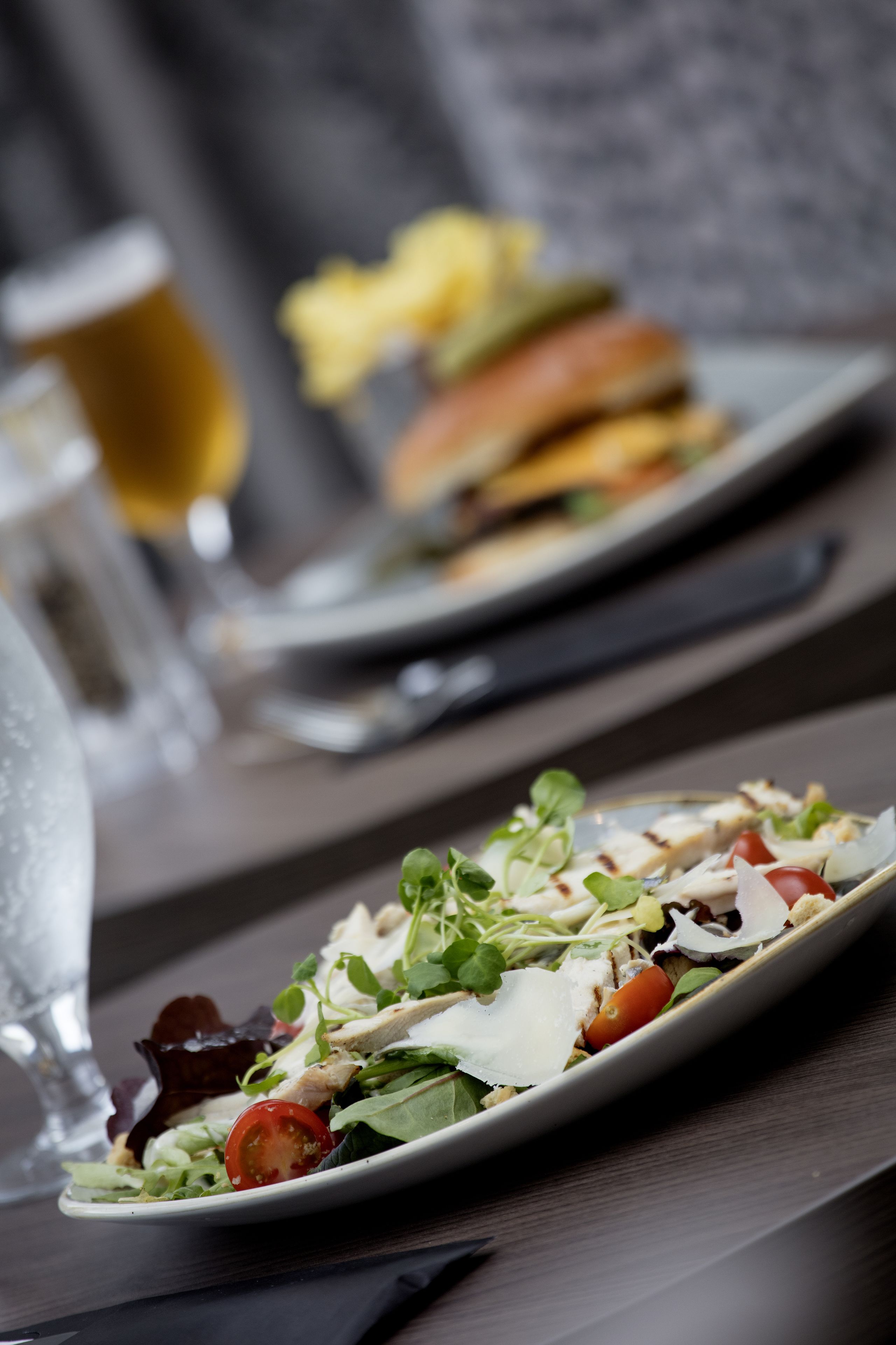 A dining table with a plate of salad, a glass of water, and a glass of beer.