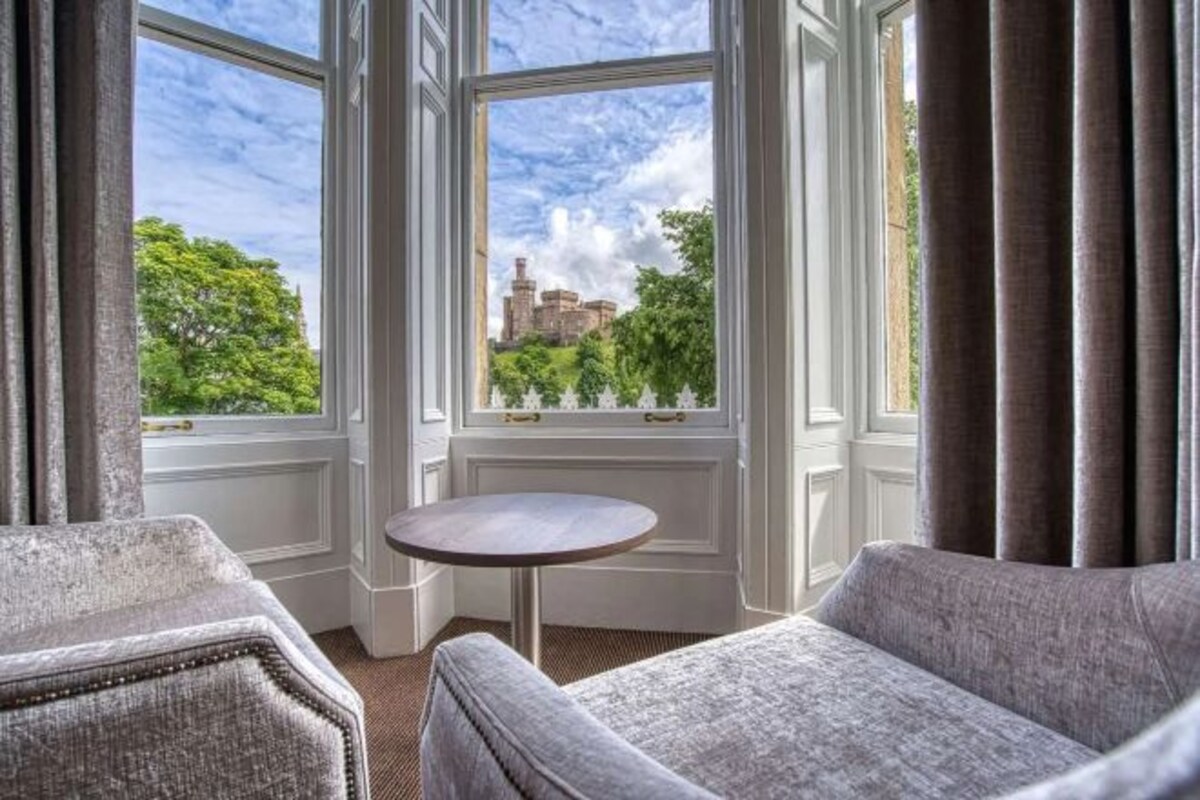 A room with a view of a historic building, a round table, and two upholstered chairs.