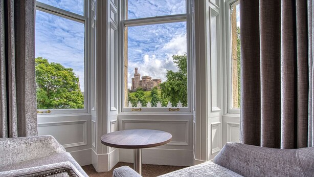 A room with a view of a castle through large windows, a round table, and two upholstered chairs. - Inverness Palace Hotel & Spa, WorldHotels Distinctive (Inverness)