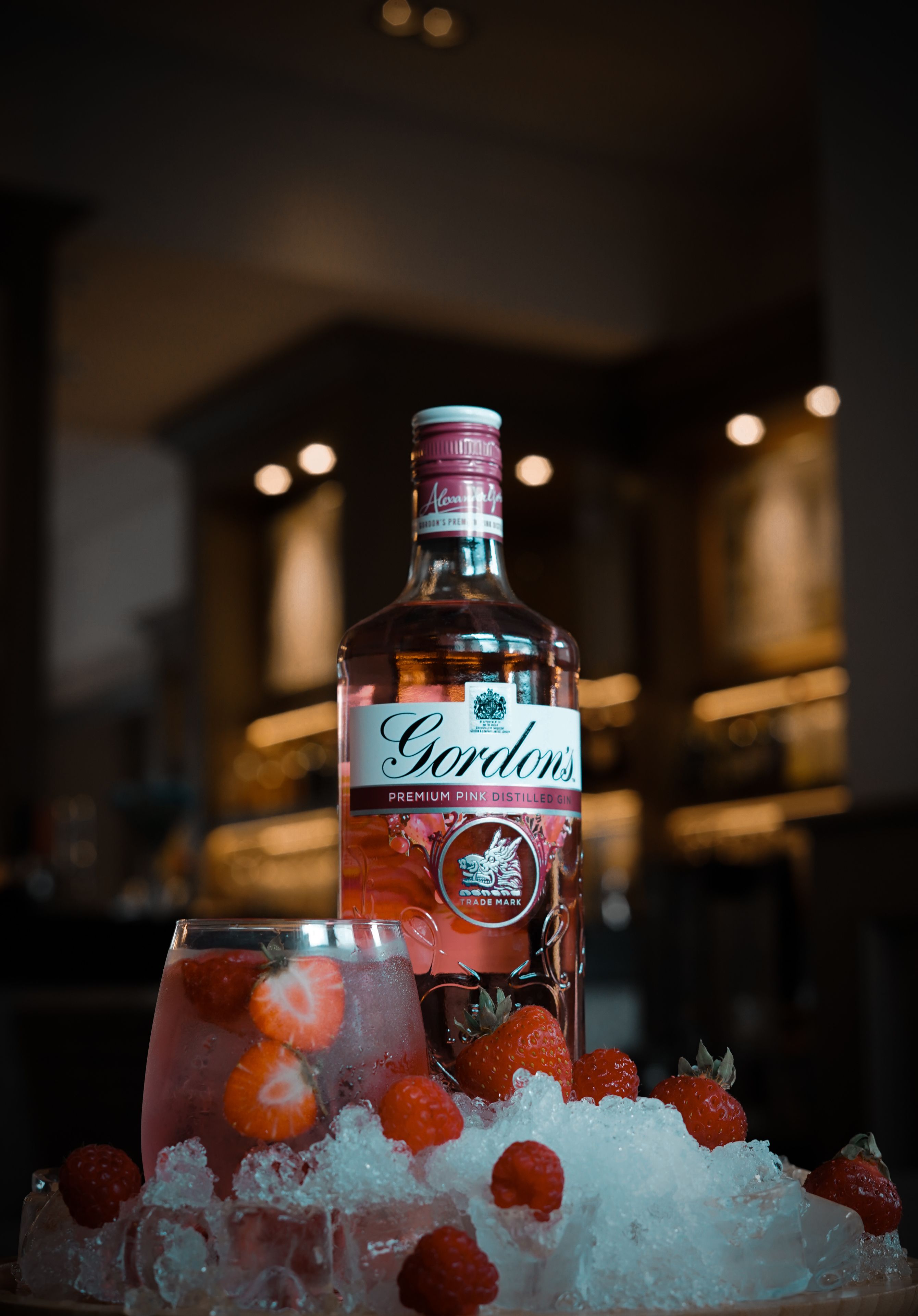 A bottle of Gordon's Premium Pink Distilled Gin and a glass with strawberries and ice.