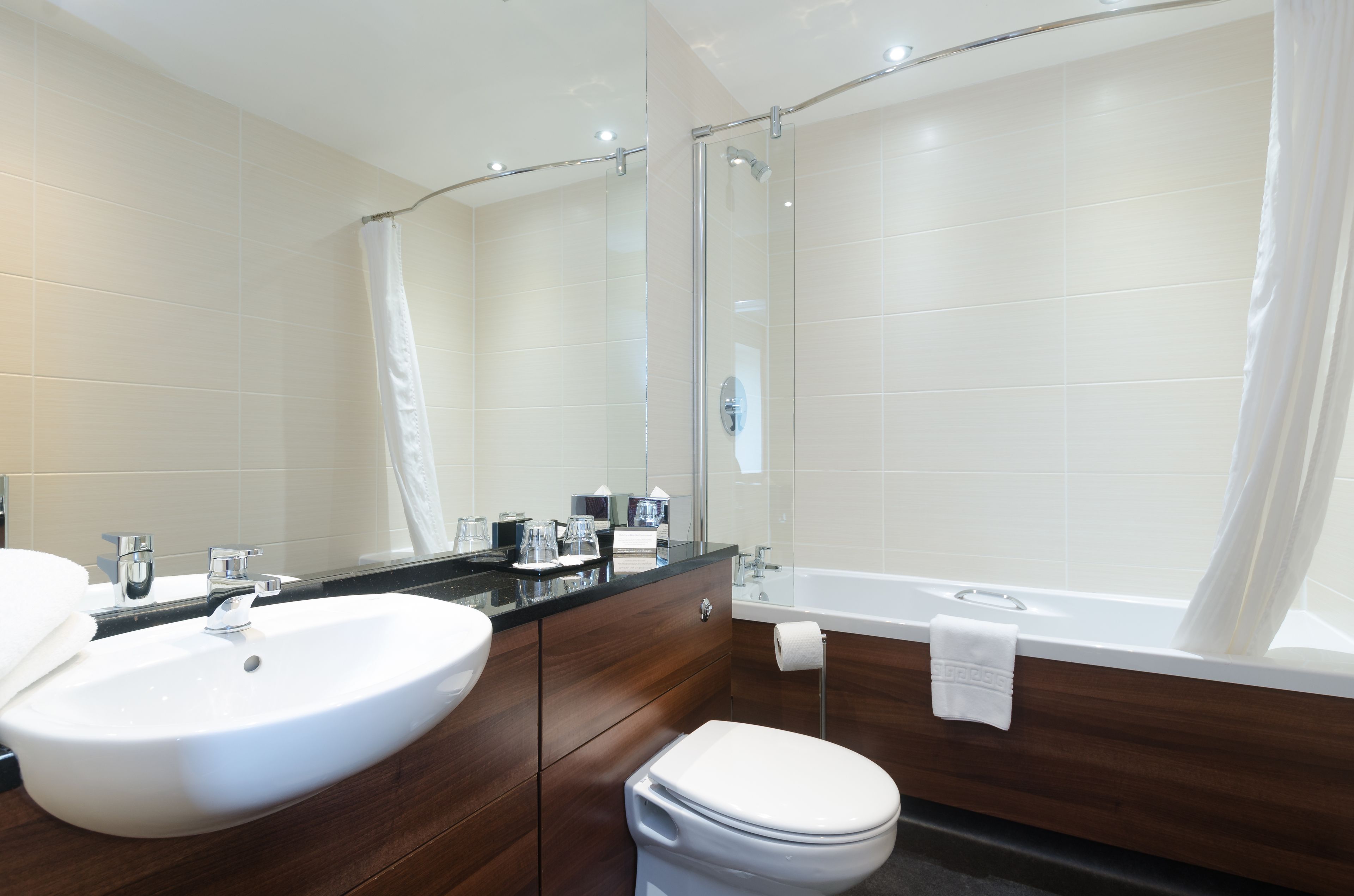 Un baño moderno con un lavamanos blanco grande, una cabina de ducha de vidrio y un mueble de tocador de madera.