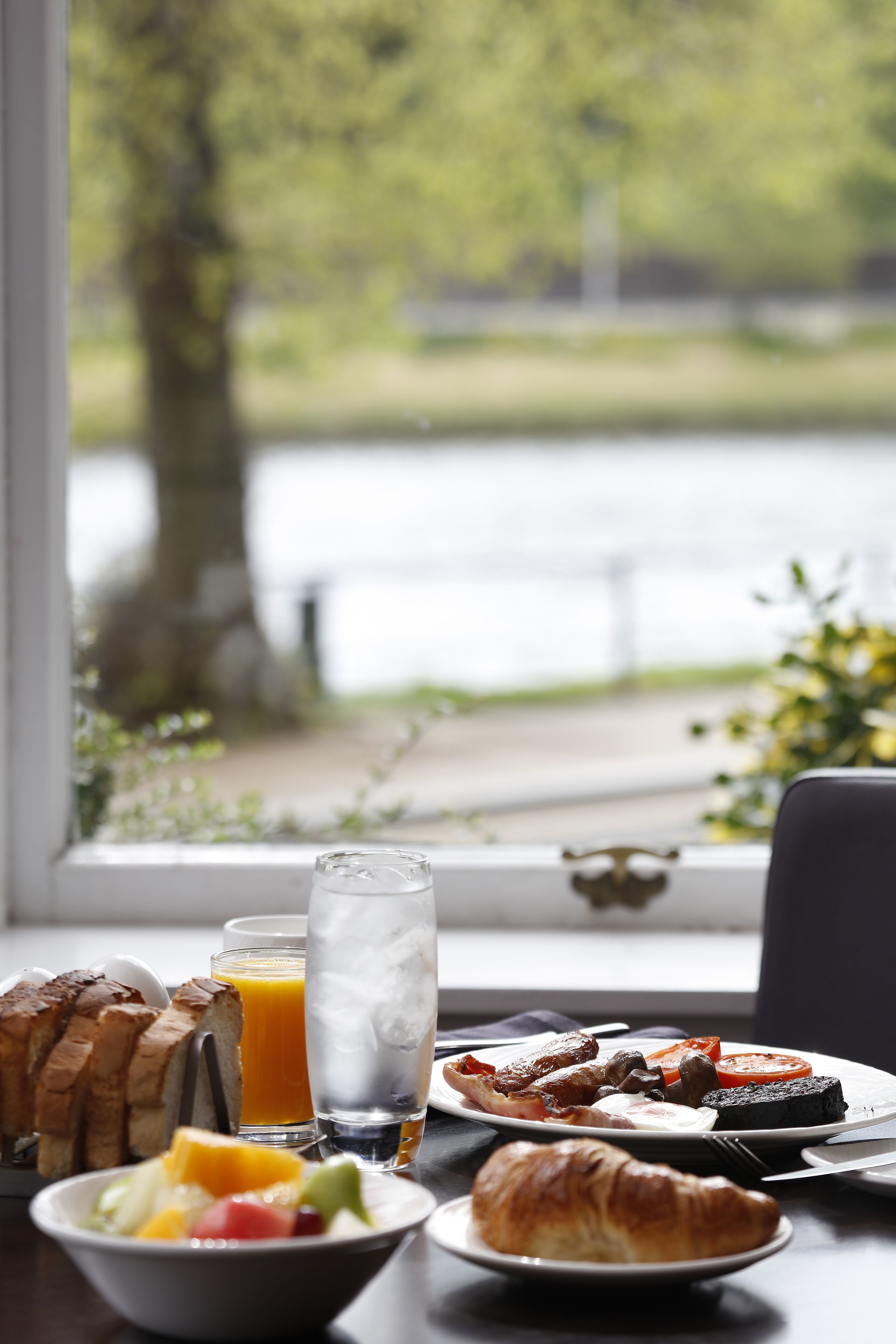 Ett frukostbord med croissanter, rostat bröd, frukt och ett glas apelsinjuice.