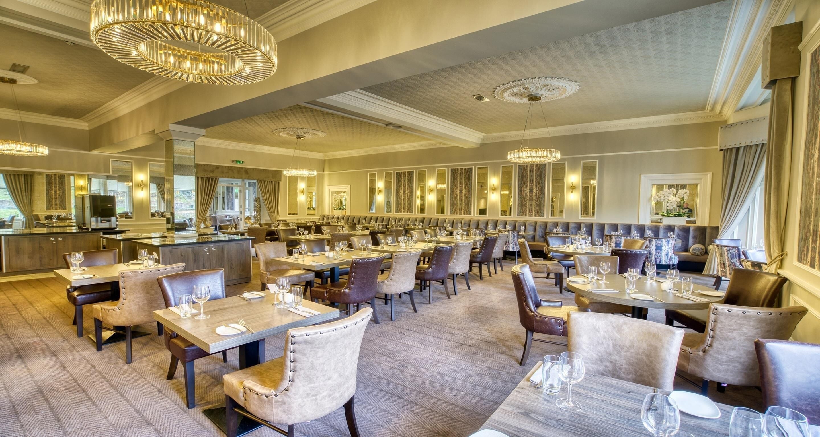 A spacious restaurant with multiple dining tables and chairs, elegant chandeliers, and a modern interior design.