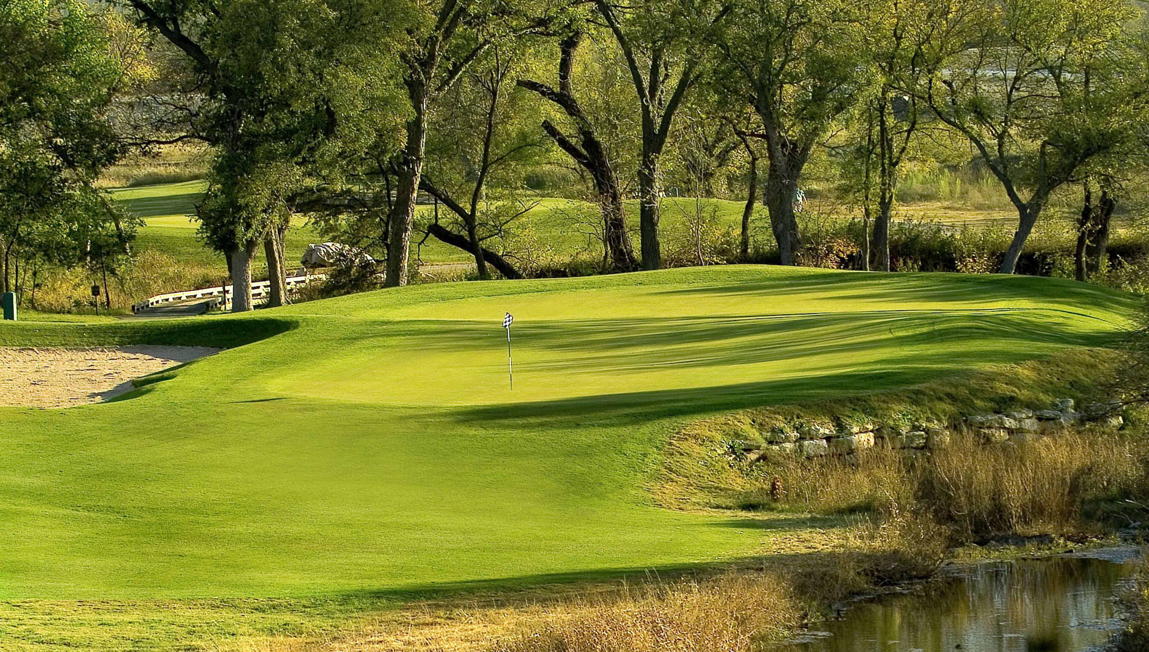A golf course with a water hazard, trees, and a stone wall.