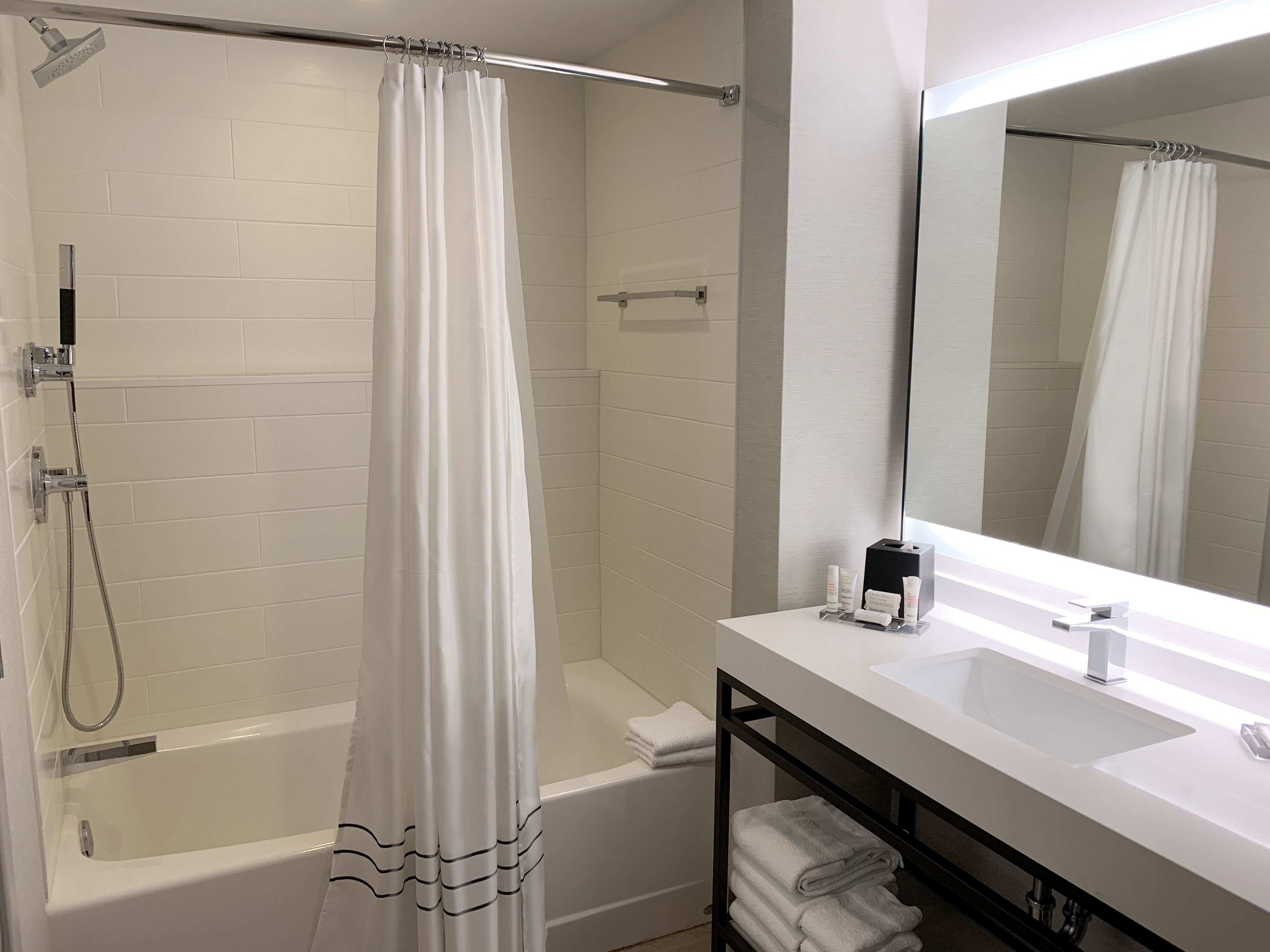 A modern bathroom with a white bathtub, a shower curtain, a large mirror, and a sink with a towel rack.