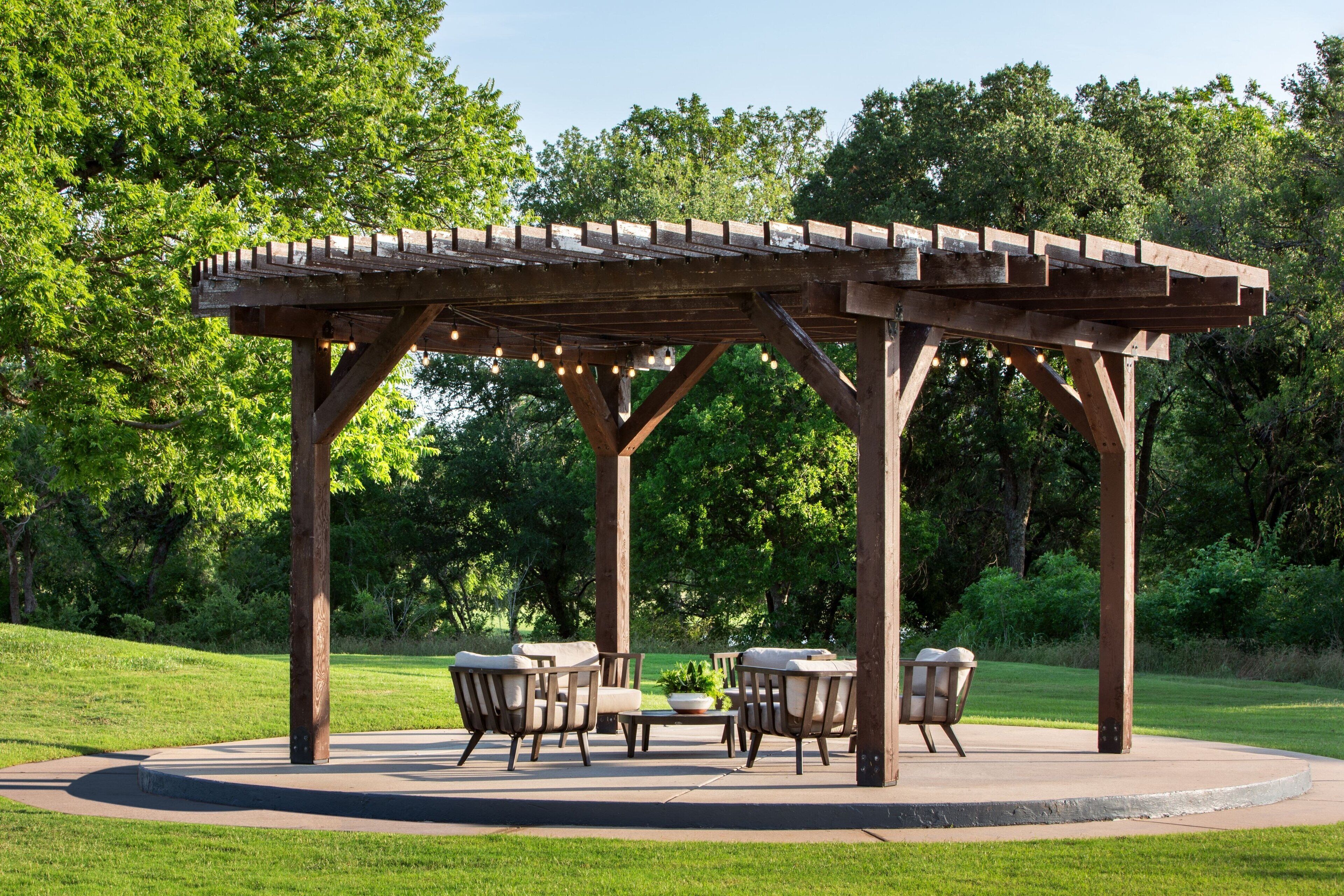 A wooden gazebo with a circular seating area, surrounded by lush greenery.