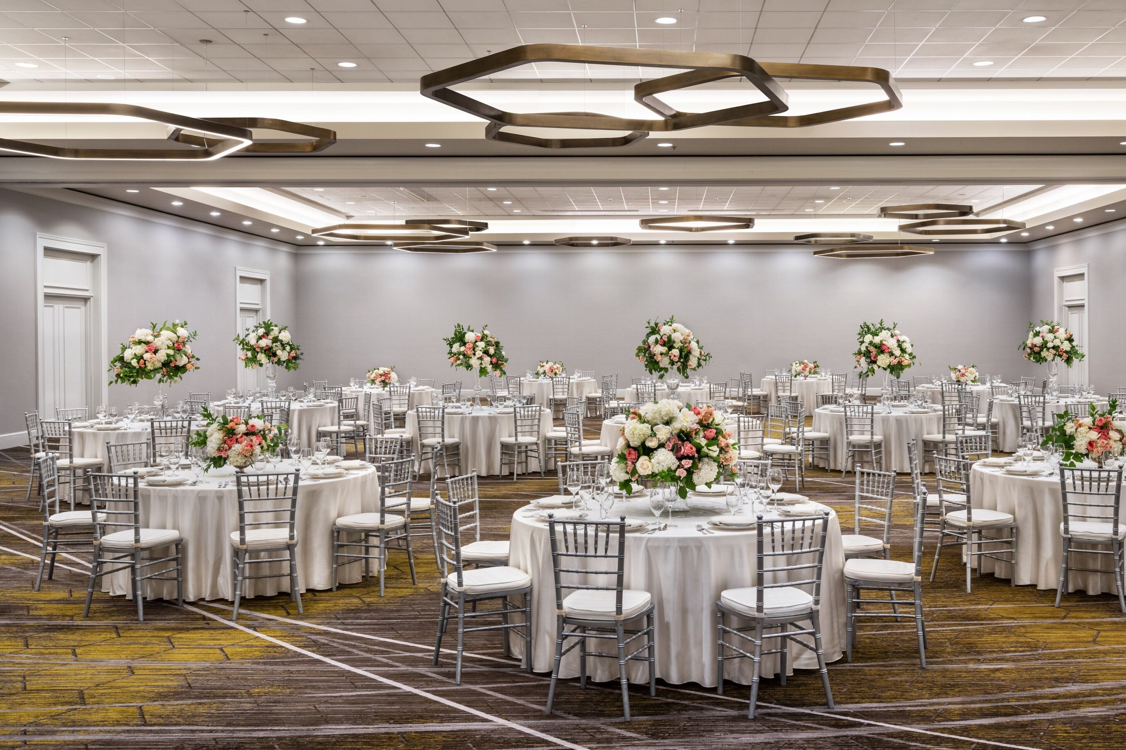 A banquet hall with round tables, white tablecloths, and floral centerpieces.