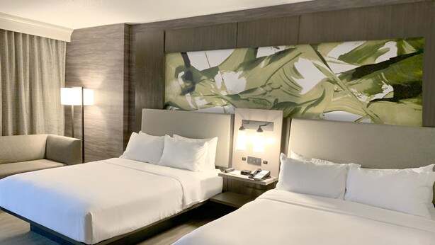 Une chambre d’hôtel avec deux lits, un canapé, une table de chevet avec une lampe et un grand tableau mural.