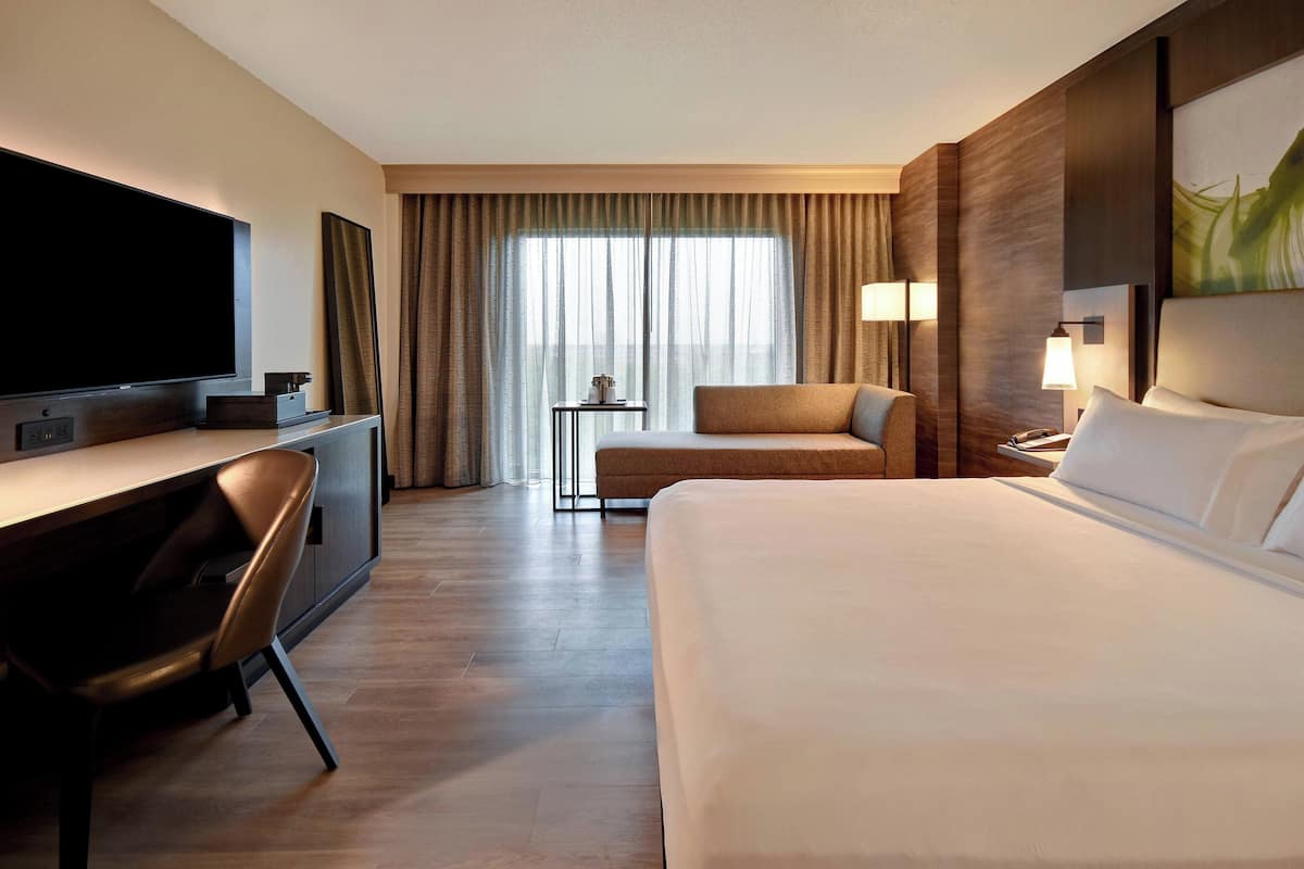 Ein Hotelzimmer mit Bett, Schreibtisch mit Stuhl, Fernseher, kleinem Tisch und Lampe.