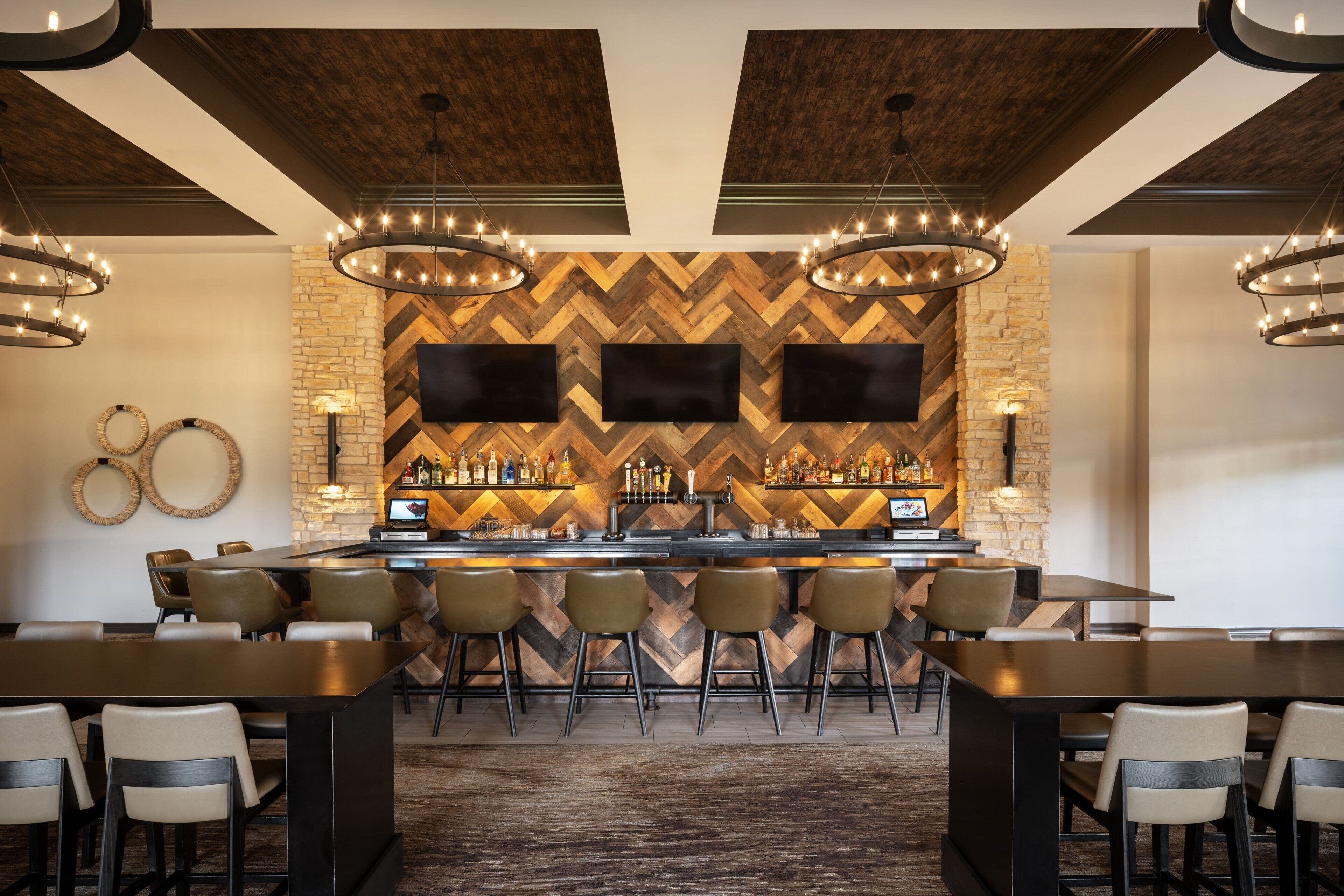 A bar area with a herringbone-patterned wall, multiple bar stools, and a central bar counter.