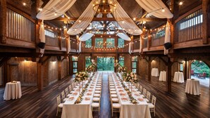 Une longue salle de banquet avec des tables et des chaises blanches, décorée de tissu blanc et illuminée de guirlandes lumineuses.