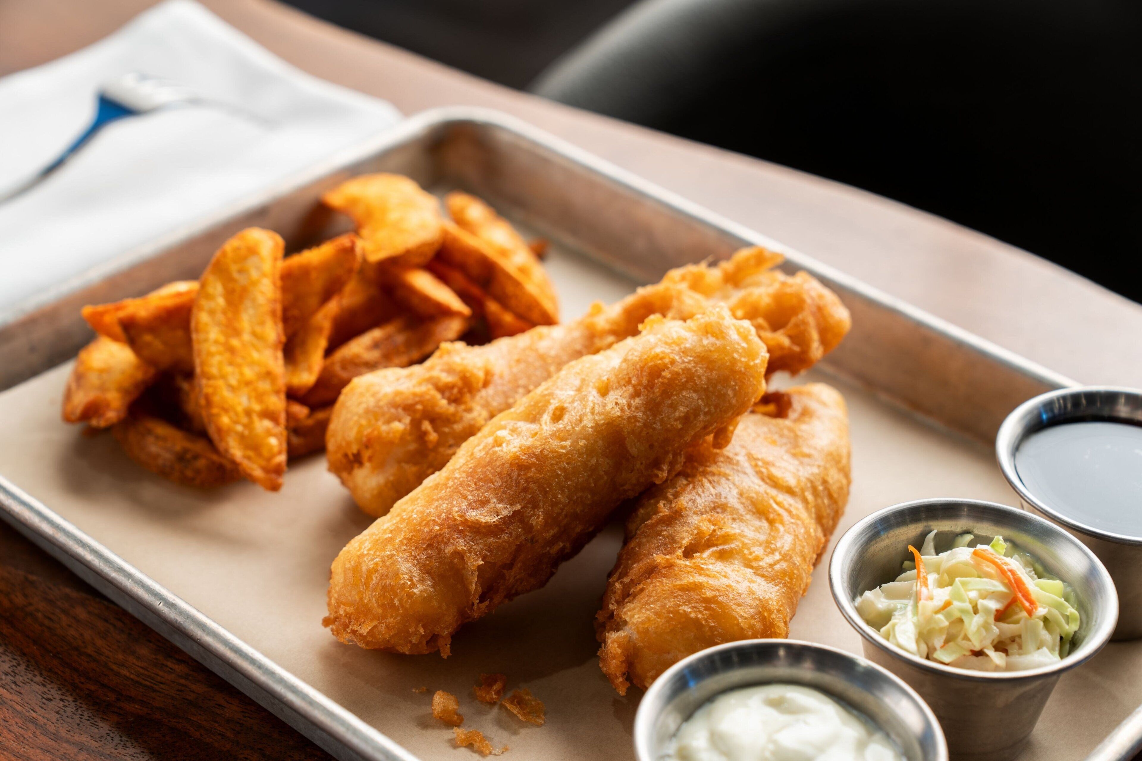 A tray with fried fish, chips, and two small containers of dipping sauces.