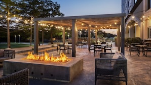 Un espace extérieur aménagé en terrasse, avec un foyer, des sièges et des guirlandes lumineuses.