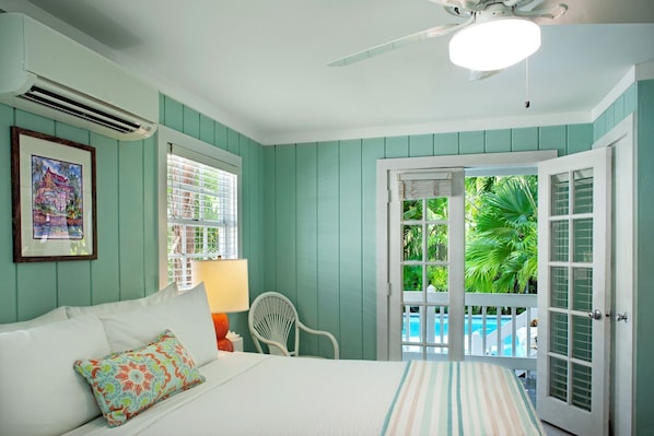 Un dormitorio con cama, una silla, una ventana con persianas y una puerta que da a un balcón con piscina.