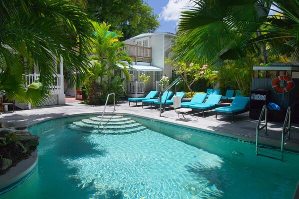 A swimming pool with blue lounge chairs, surrounded by palm trees and a wooden deck.