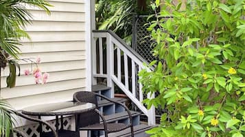 An outdoor patio with a table and chairs, surrounded by lush greenery and a wooden fence.