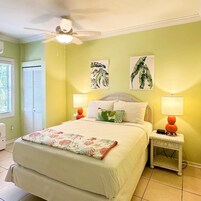 A bedroom with a bed, two wall-mounted lamps, a ceiling fan, and two framed botanical prints.