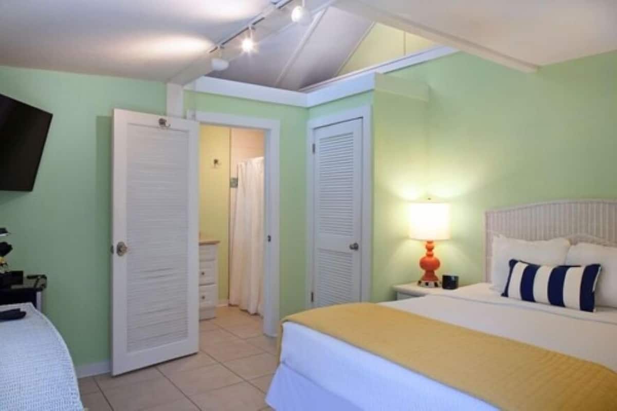 Una habitación de hotel con cama, mesita de noche, lámpara y televisión en la pared.