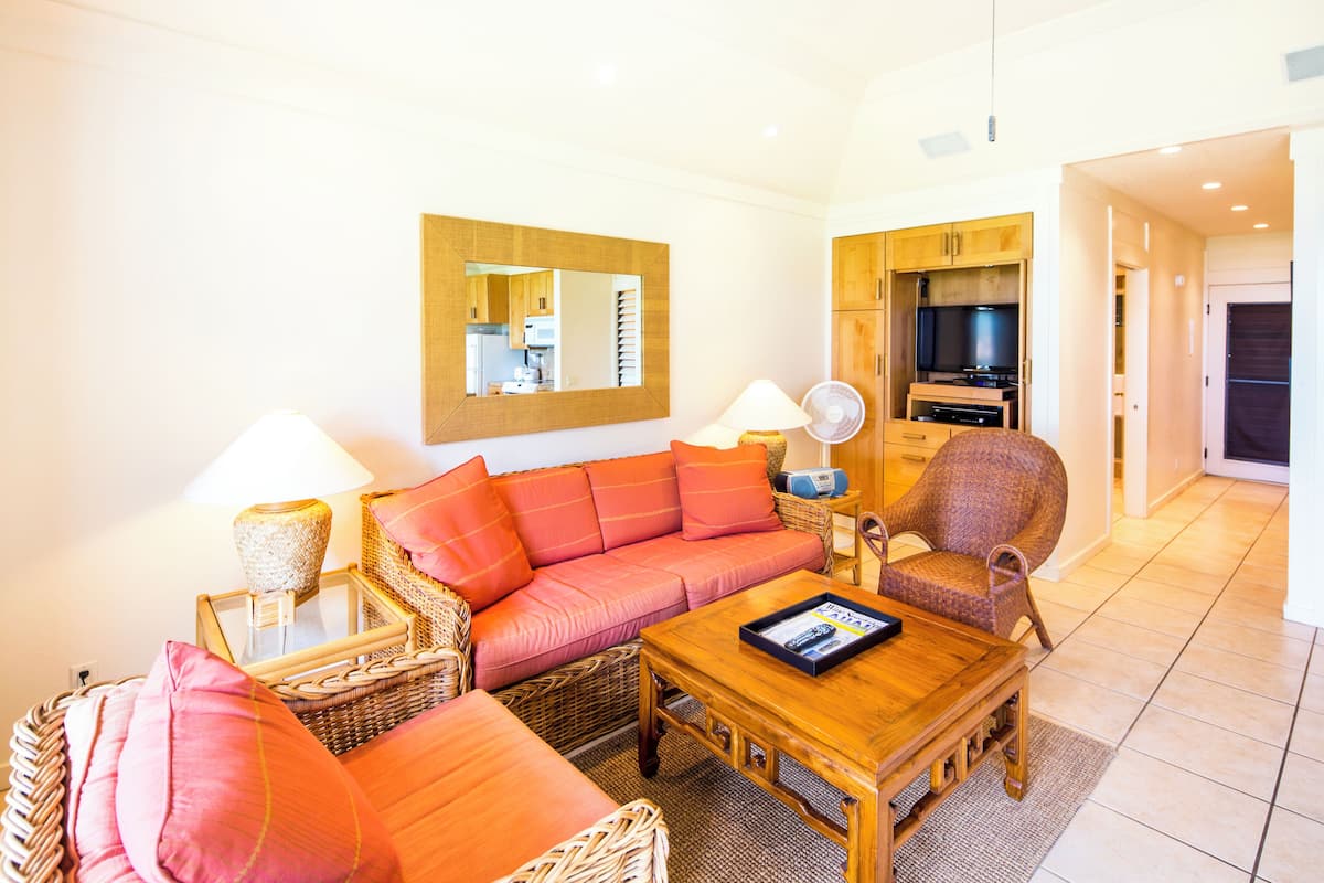 A living room with a sofa, a coffee table, a chair, a lamp, a mirror, and a television.