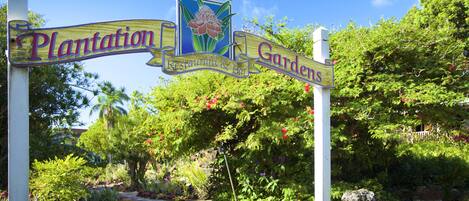 A sign for Plantation Gardens with a floral design and a pathway leading through lush greenery.