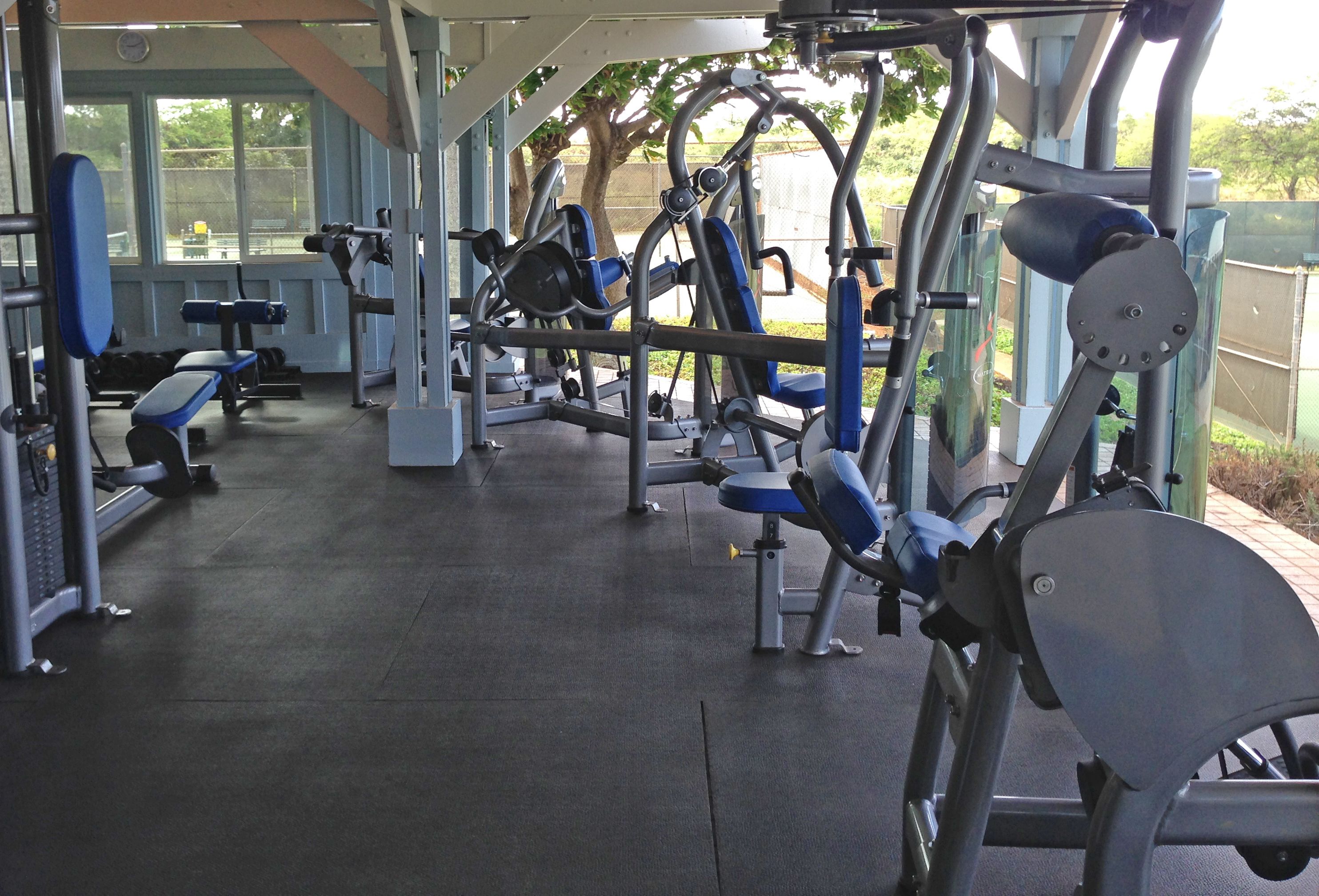 A gym with various exercise machines, benches, and a large window providing natural light.