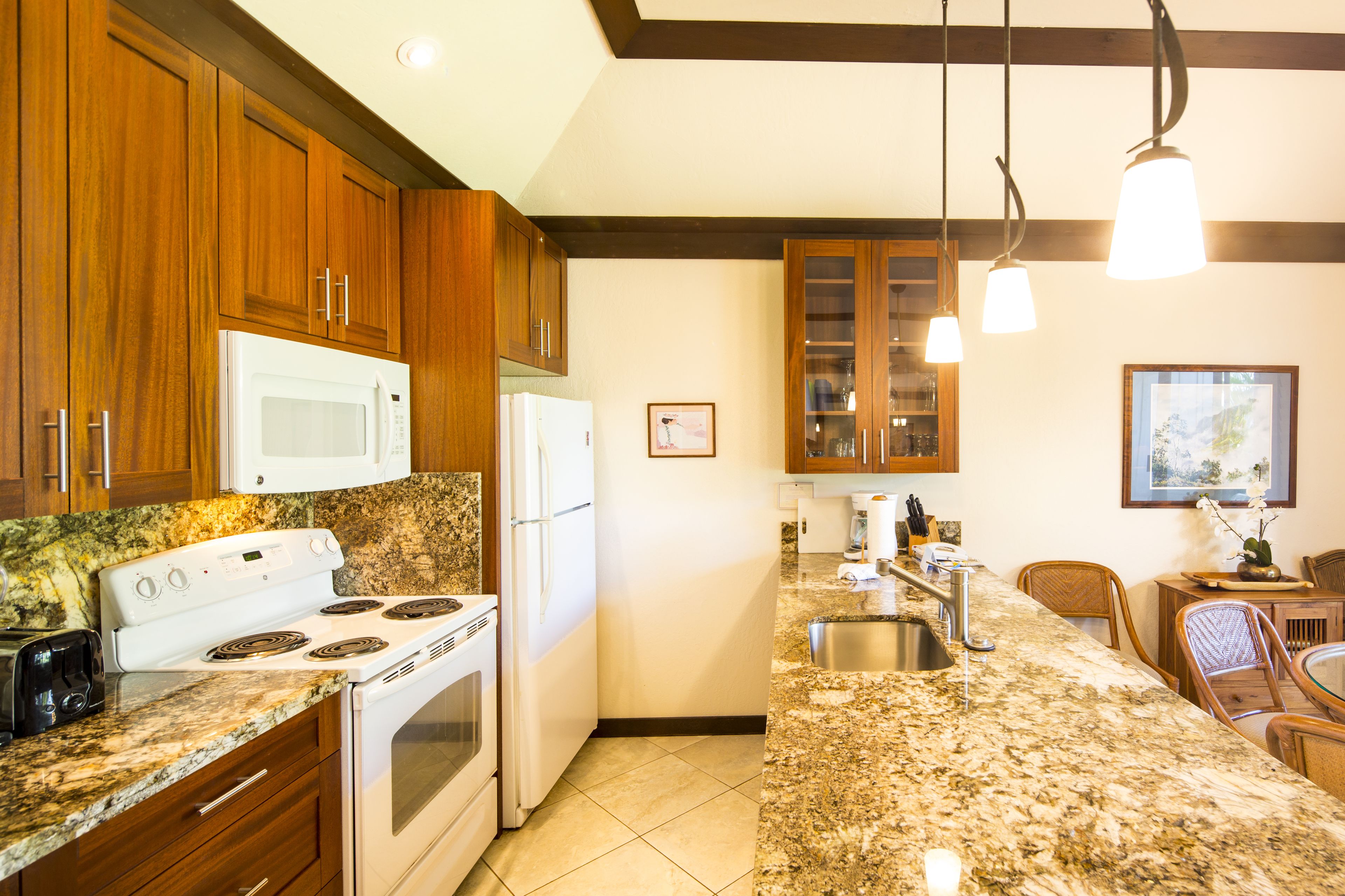 A kitchen with wooden cabinets, a granite countertop, a stove, a microwave, and a sink.