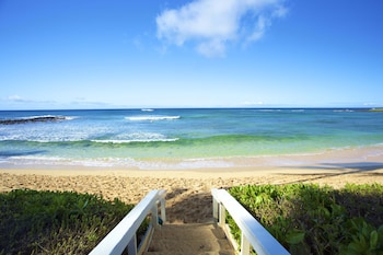 A hotel with a pool, surrounded by palm trees and greenery. at Castle Kiahuna Plantation & Beach Bungalows