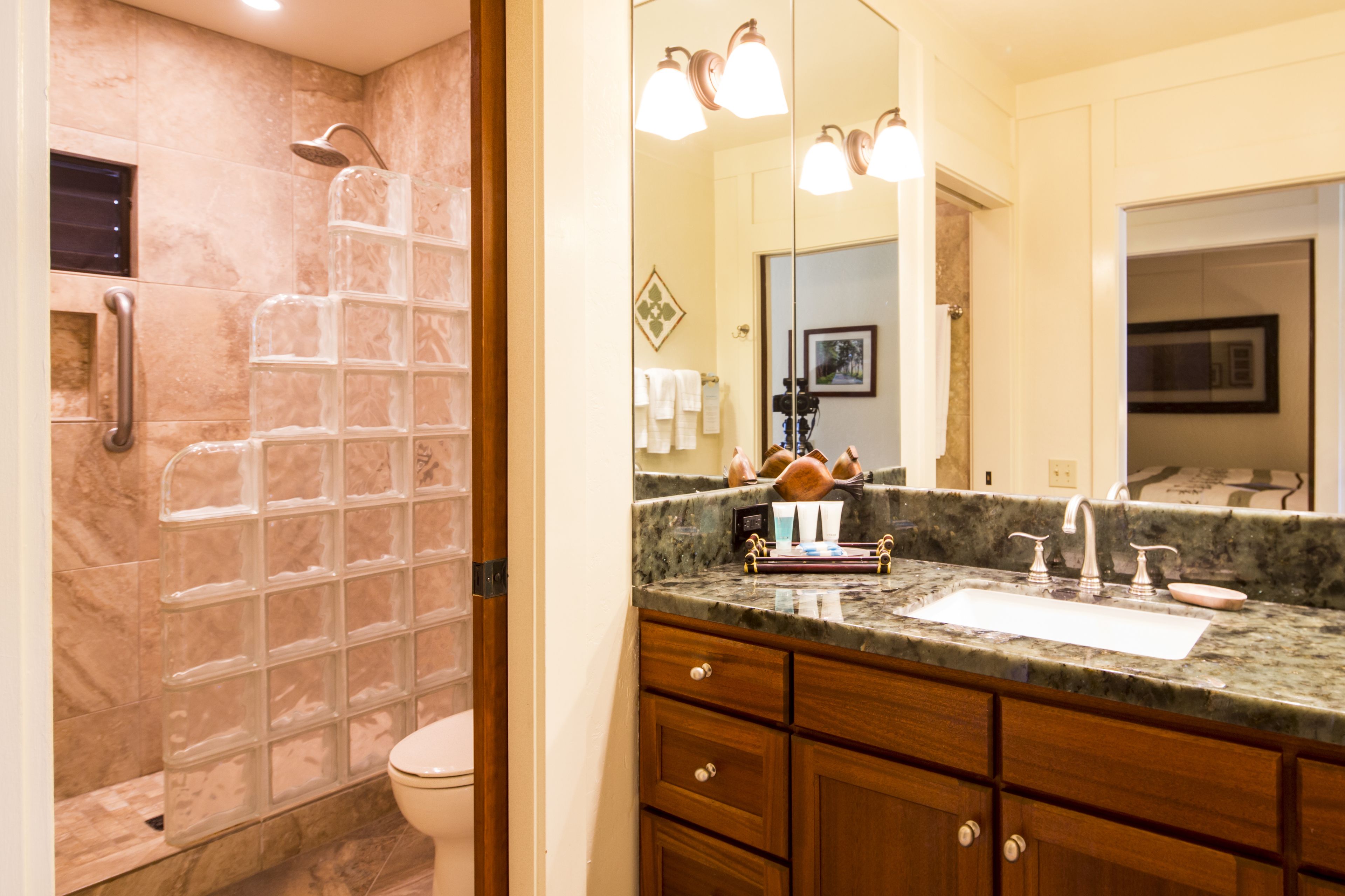 A bathroom with a glass shower enclosure, a marble countertop, and a wooden vanity with drawers.