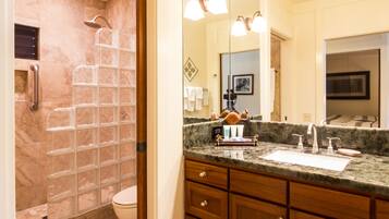 A bathroom with a glass shower enclosure, a marble countertop, and a wooden vanity with drawers.