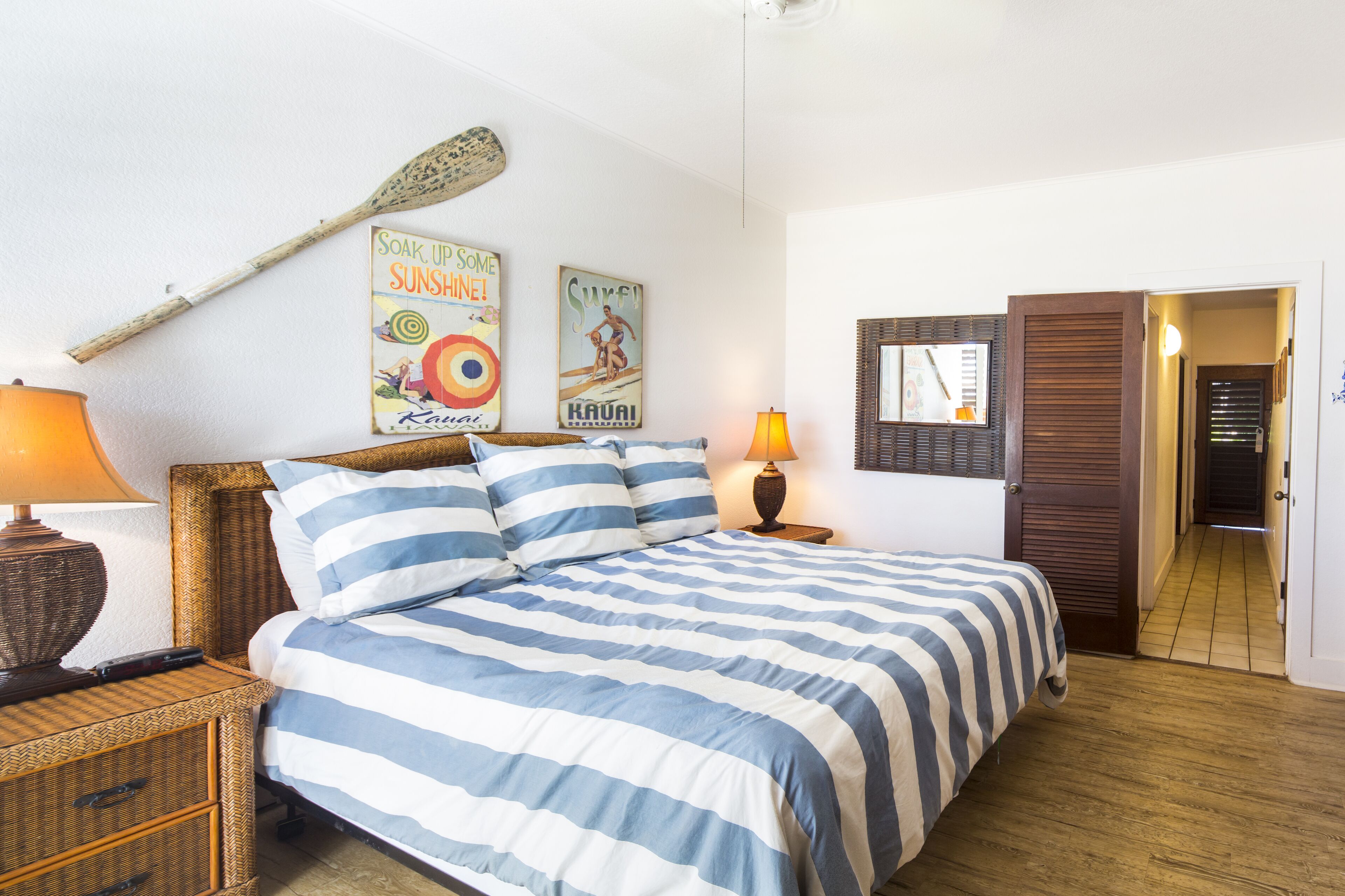Ein Schlafzimmer mit einem Bett, zwei Nachttischen, Holzboden und Wanddekorationen, darunter ein Poster und ein Stand-Up-Paddle.