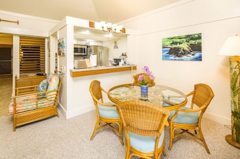 A bedroom with a bed, two nightstands, a wooden floor, and wall decorations including a poster and a paddleboard. at Castle Kiahuna Plantation & Beach Bungalows