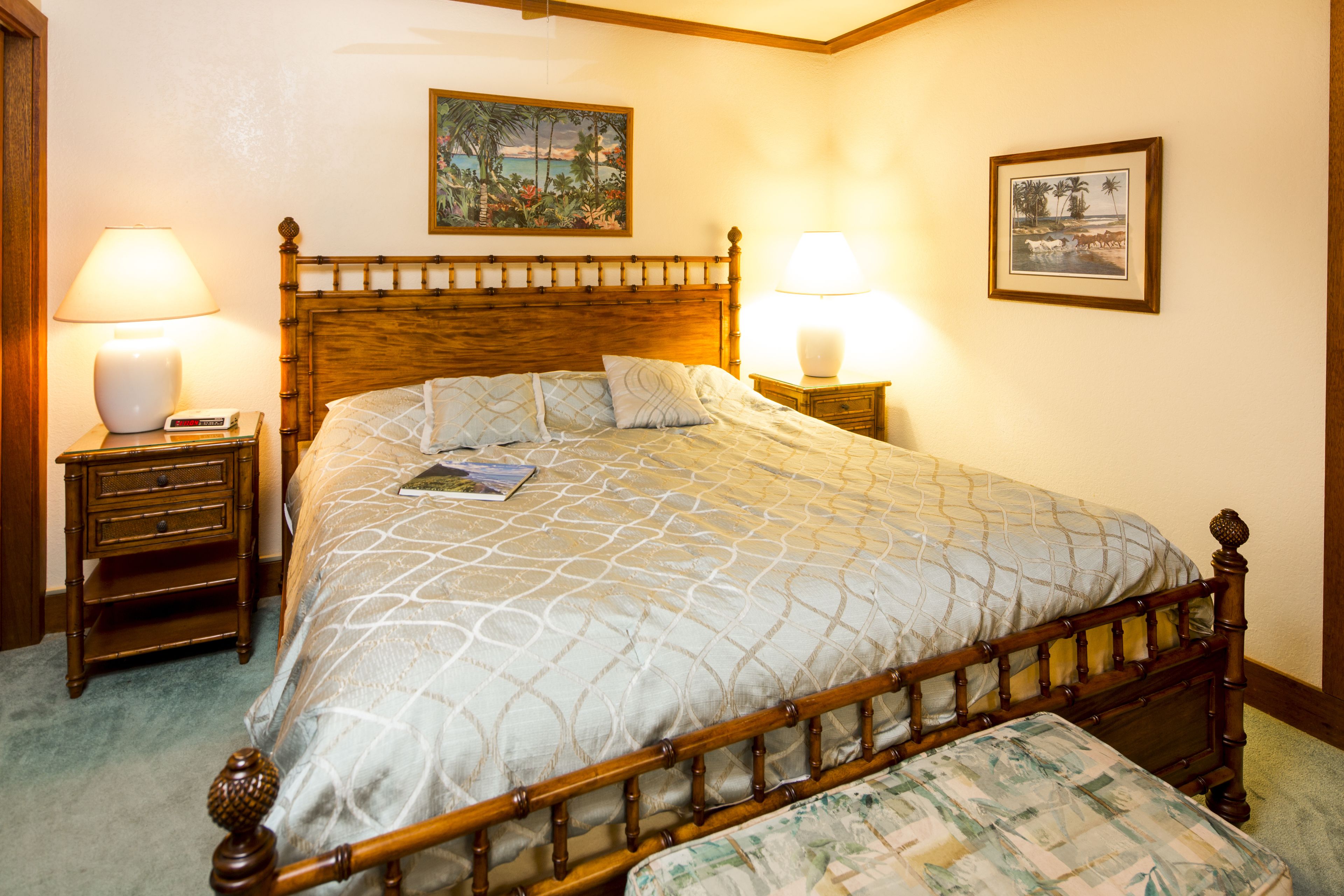 A neatly made bed with a wooden headboard, two bedside tables with lamps, and a painting on the wall.