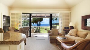 A spacious living area with a large window overlooking a tropical landscape, a comfortable seating arrangement, and a kitchen counter.