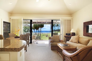A golf course with palm trees and a building with a balcony overlooking the ocean. at Castle Kiahuna Plantation & Beach Bungalows
