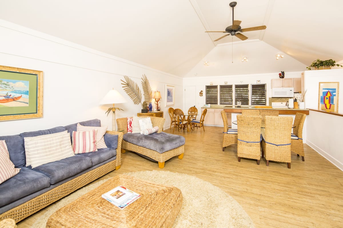 A spacious living area with a sofa, ottoman, wicker chairs, and a dining set.