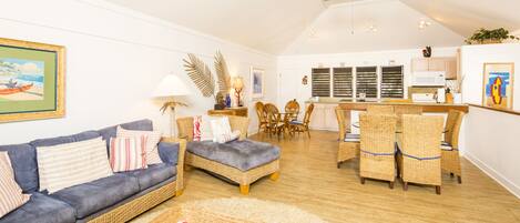 A spacious living area with a sofa, ottoman, wicker chairs, and a dining set.