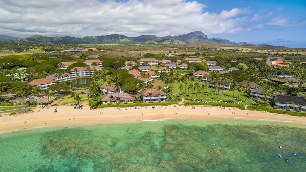 Un resort costero con villas frente a la playa, aguas turquesas cristalinas y exuberante vegetación.
