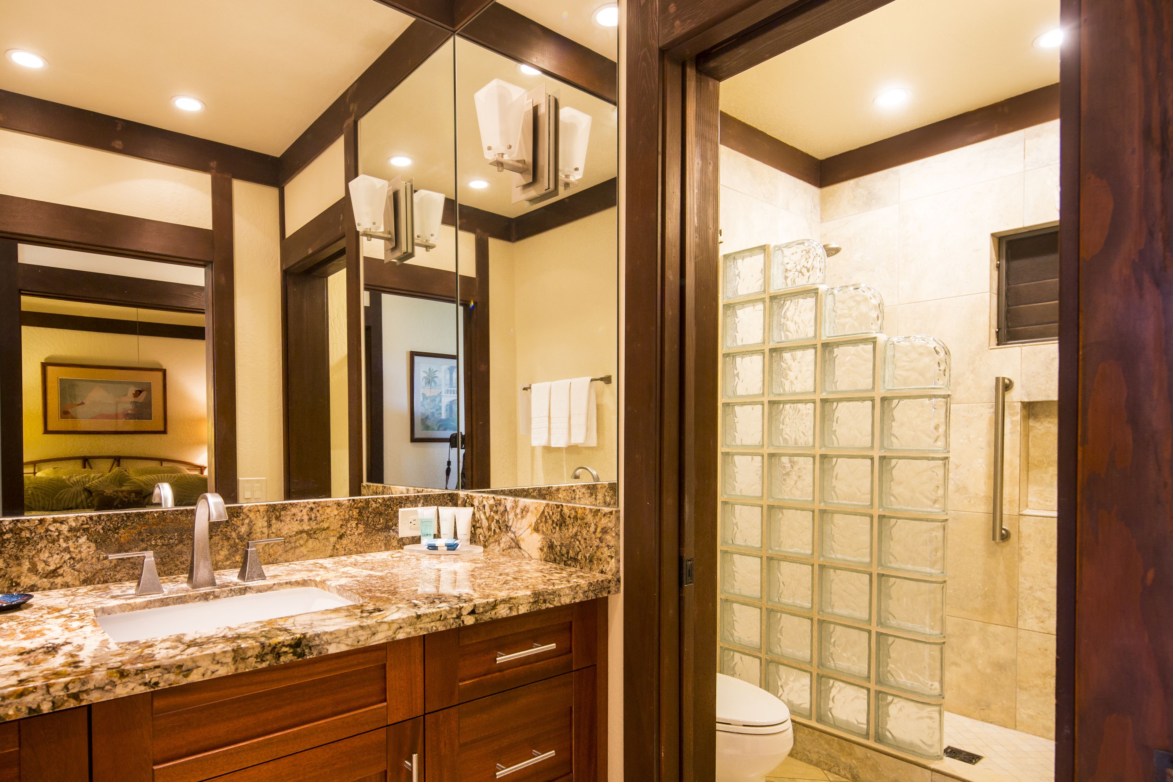 A bathroom with a granite countertop, wooden cabinets, a large mirror, and a glass shower enclosure.