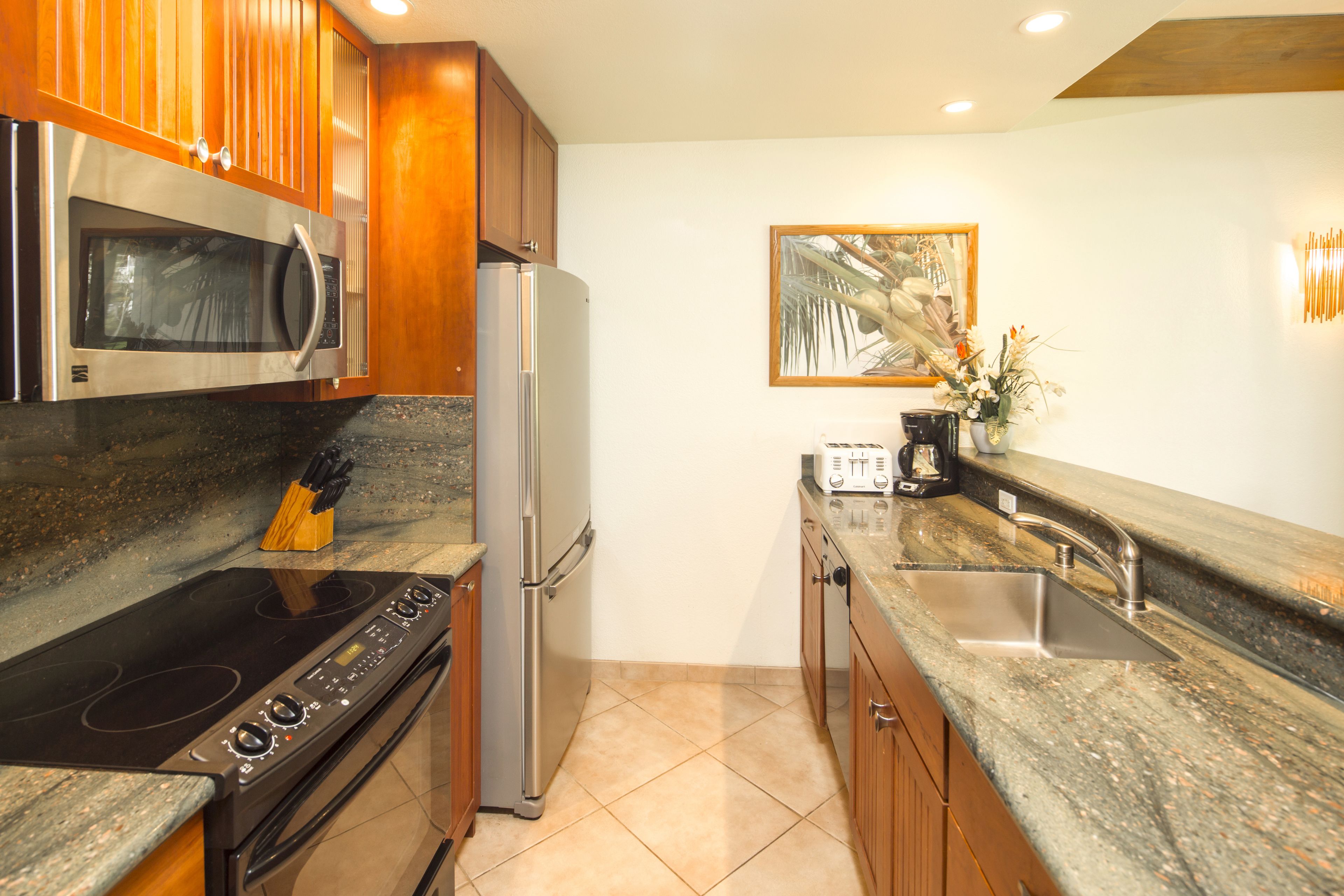 A modern kitchen with a stainless steel refrigerator, a microwave, an induction cooktop, and wooden cabinets.