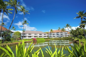 A spacious living area with a large window overlooking a tropical landscape, a comfortable seating arrangement, and a kitchen counter. at Castle Kiahuna Plantation & Beach Bungalows