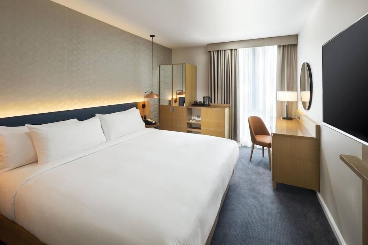 Une chambre d’hôtel avec un grand lit, un bureau, une chaise, une télévision et un miroir.