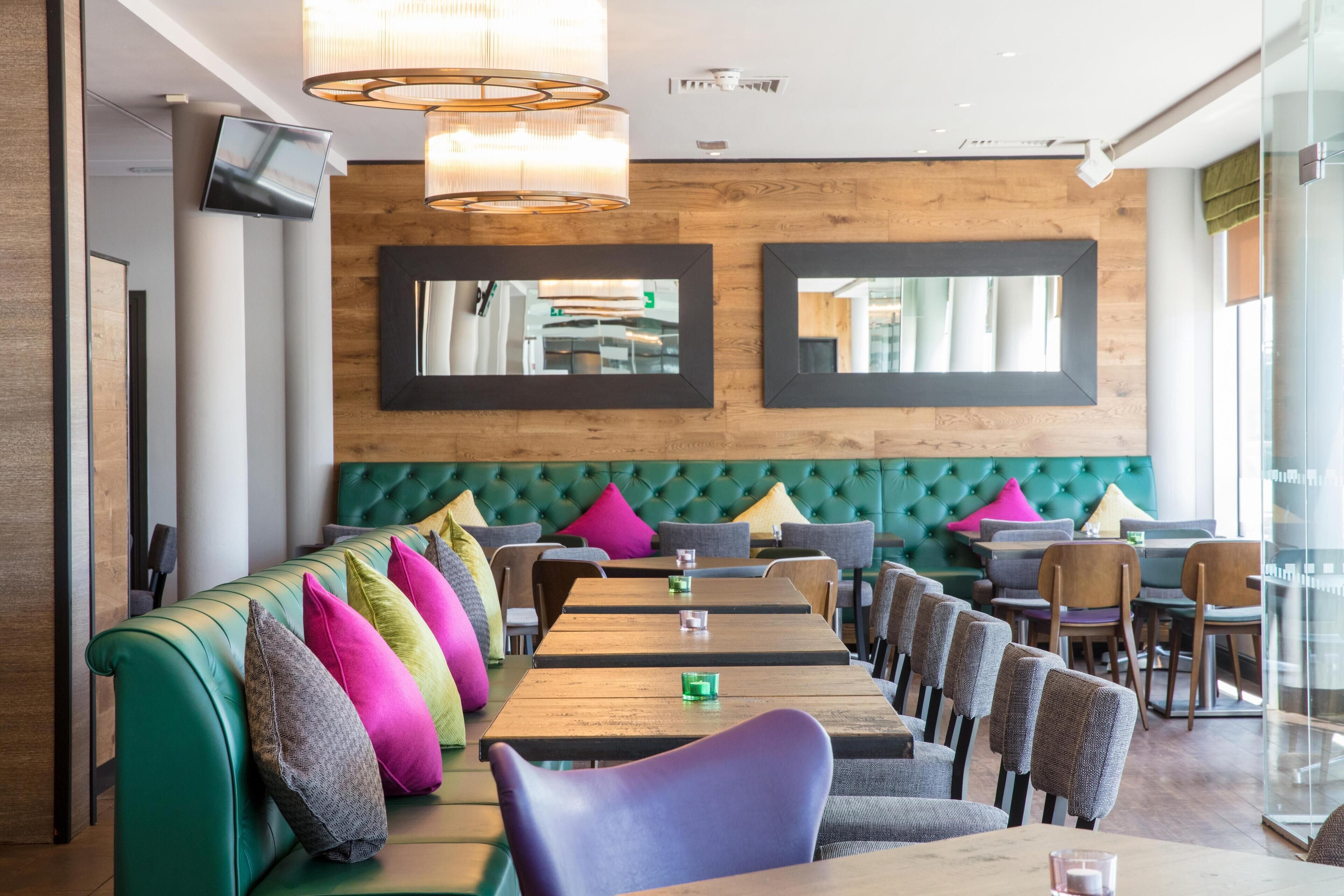 Un ristorante con una panca imbottita in verde, tavoli e sedie in legno.