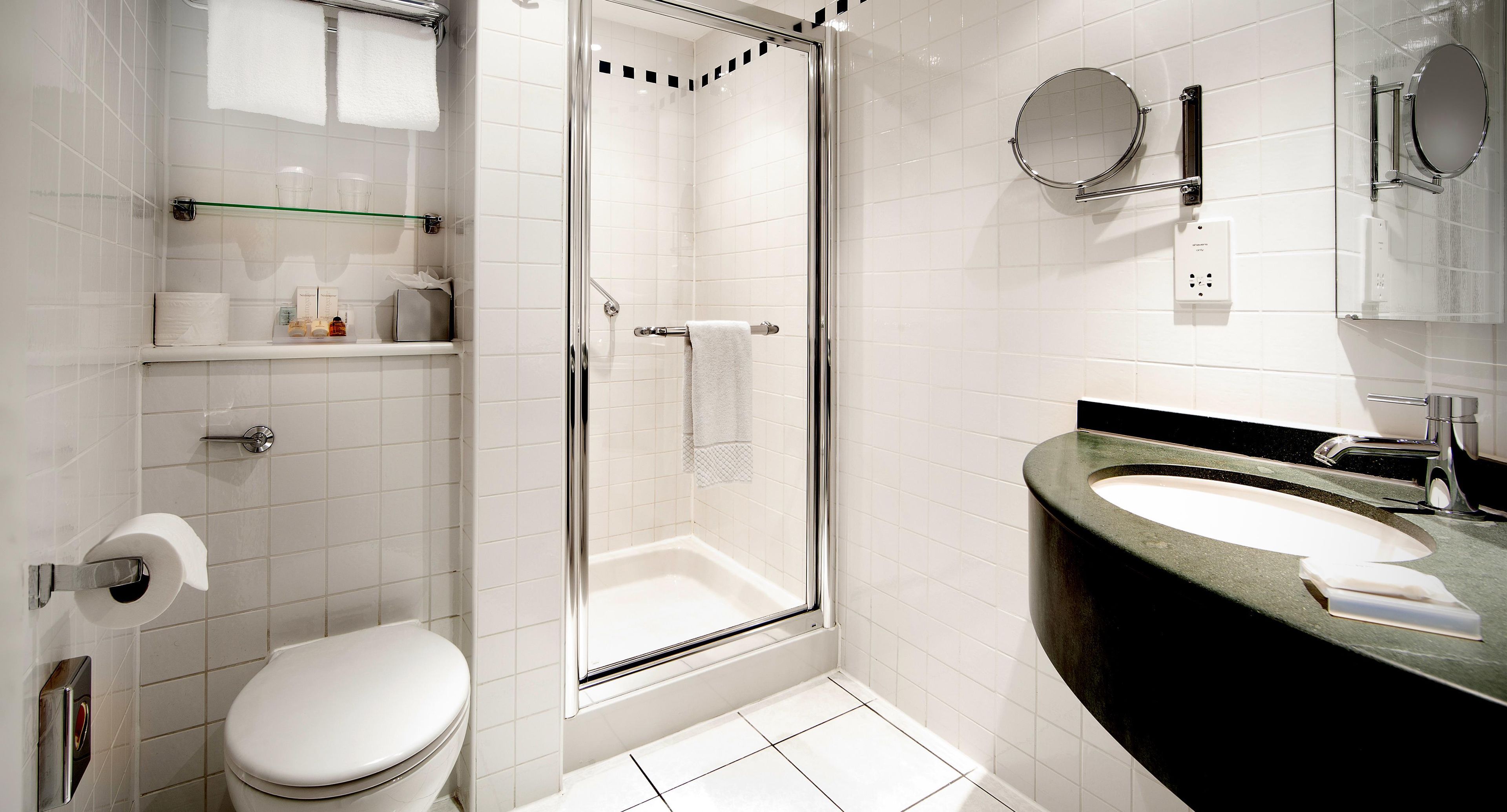 Een moderne badkamer met een douchecabine van glas, een wit toilet, een zwart wastafelmeubel en een spiegel.